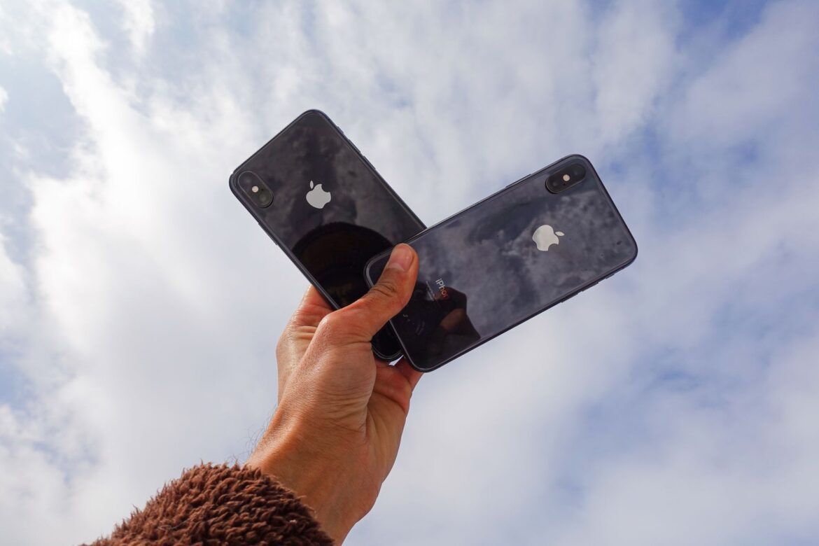 Primer plano de una mano sosteniendo dos smartphones contra un cielo nublado, mostrando la tecnología moderna.