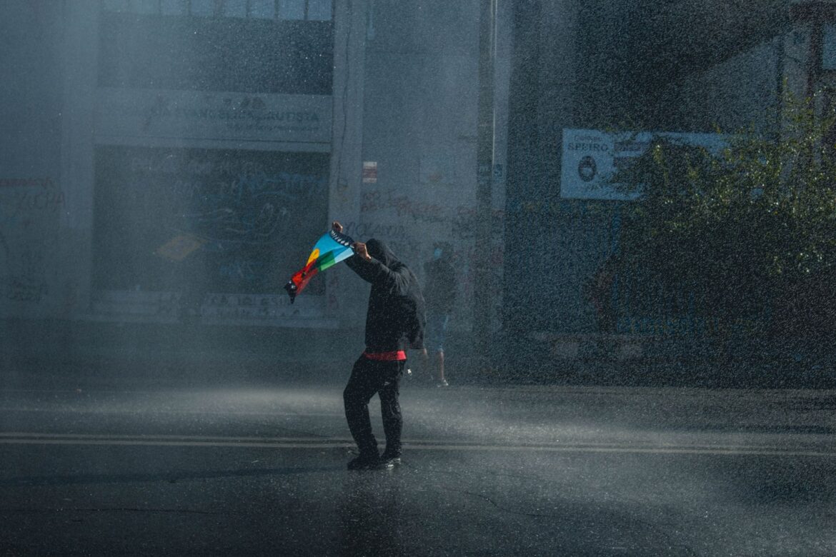 Un solo manifestante sosteniendo una bandera en una calle lluviosa, simbolizando activismo y resiliencia en Valparaíso, Chile.
