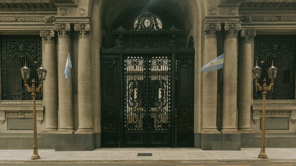 Elegante entrada del Palacio San Martín, Buenos Aires, con puertas ornamentadas y banderas argentinas.