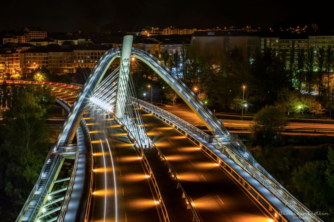 Majestuosa vista nocturna del iluminado Puente del Milenio en Ourense, España, que muestra las luces urbanas y la belleza arquitectónica.