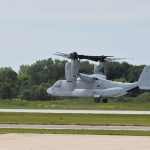 Una aeronave militar MV-22 Osprey aterrizando en la pista de un aeródromo boscoso.