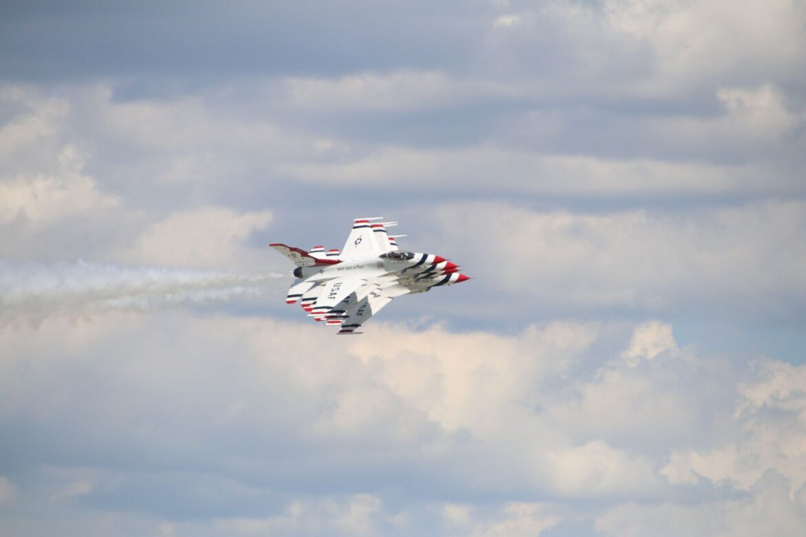Imagen dinámica de un avión Thunderbirds de la Fuerza Aérea de EE. UU. volando a través de un cielo nublado, mostrando velocidad y precisión en las maniobras aéreas.