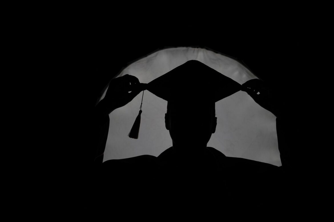 Silueta de un graduado ajustando su gorro en un ambiente dramático y oscuro.