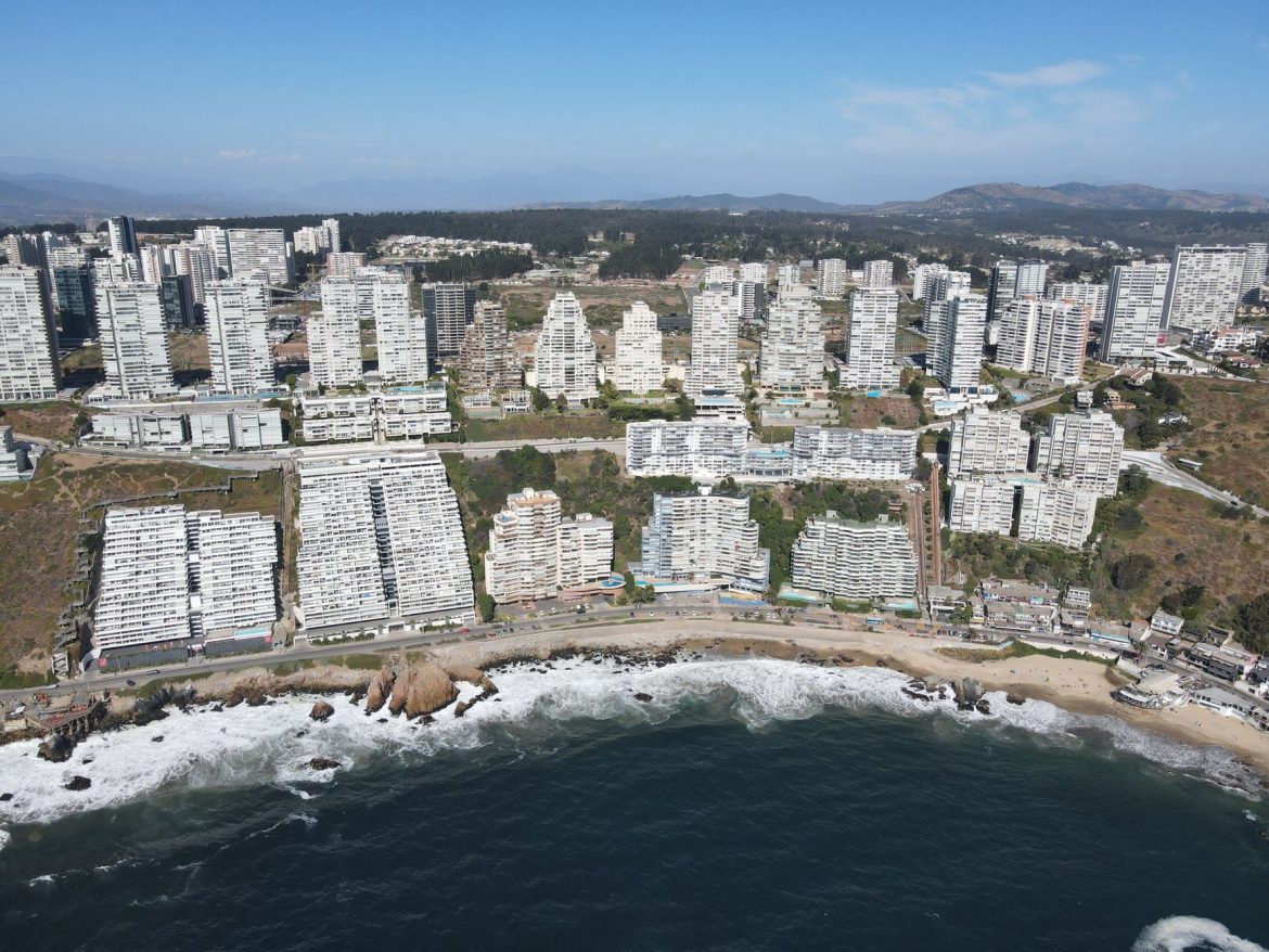 Impresionante fotografía aérea de un paisaje urbano costero con modernos rascacielos, olas del océano y una atmósfera vibrante.