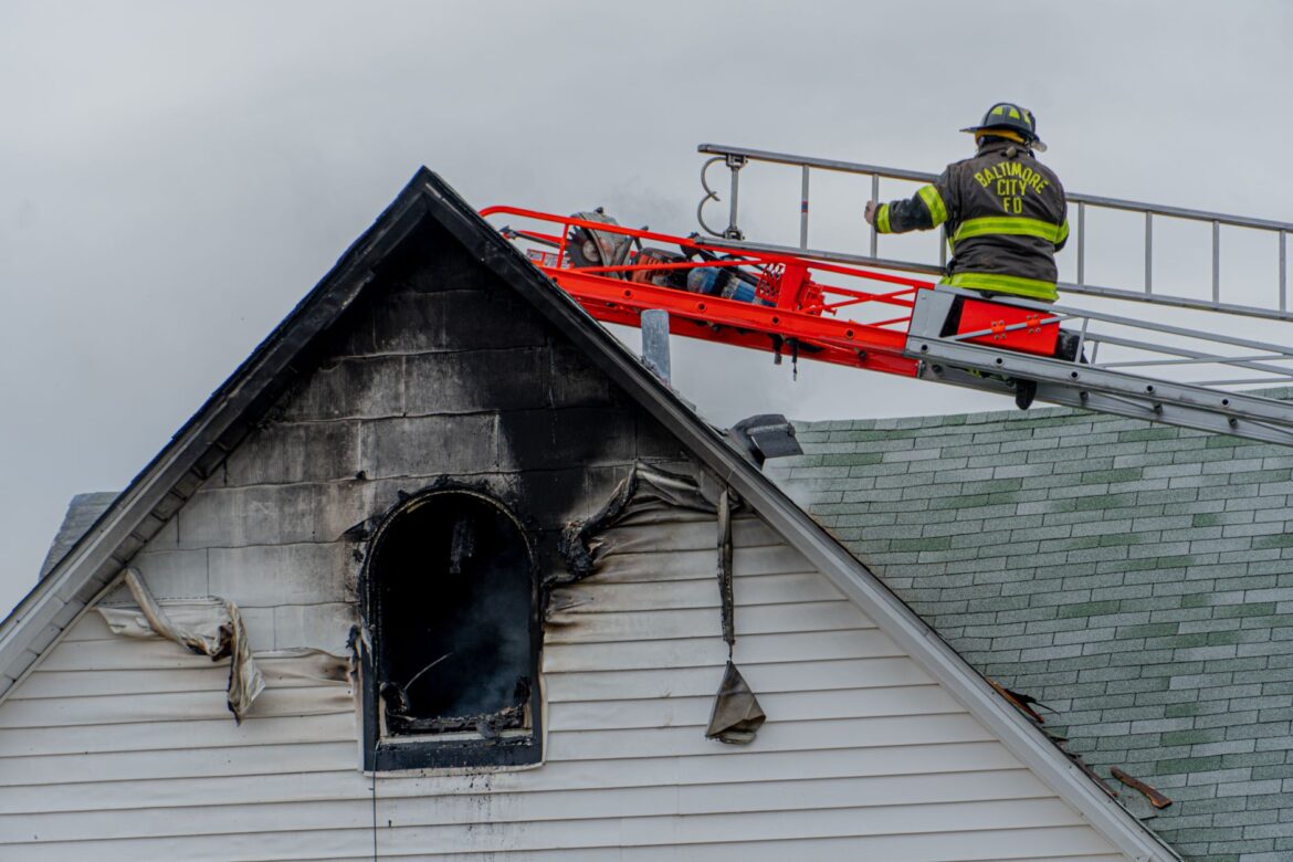Bombero en la escalera apagando un incendio en el techo de una vivienda en la ciudad de Baltimore.