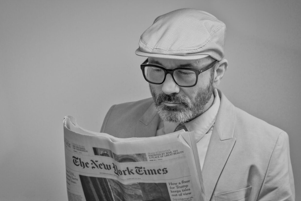 Un hombre con traje, usando gafas y una gorra, lee The New York Times.