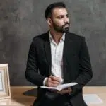 Consultor masculino seguro toma notas, rodeado de documentos legales en una oficina moderna.